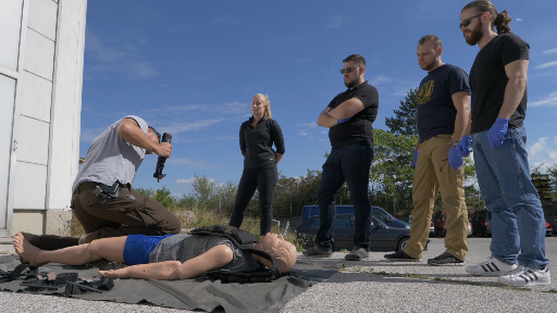 Ein maßgeschneidertes Training für Bodyguards, Personenschützer und ähnliche Berufsgruppen ist von entscheidender Bedeutung, um ihren spezifischen Anforderungen gerecht zu werden. Neben dem Basic Life Support Training liegt ein besonderes Augenmerk auf traumatischen Verletzungen, insbesondere gewaltsamen traumatischen Verletzungen wie Schuss-, Stich- und Schnittverletzungen. Hier sind die Gründe, warum ein solches Training unerlässlich ist:  Arbeitsumgebung und Aufgaben: Bodyguards, Personenschützer und PSOs operieren in herausfordernden und gefährlichen Umgebungen, in denen sie potenziellen Gewaltsituationen ausgesetzt sind. Daher müssen sie in der Lage sein, auf traumatische Verletzungen vorbereitet zu sein, denen sie in ihrem Arbeitsalltag begegnen könnten. Das Training muss daher speziell auf ihre spezifischen Aufgaben und die damit verbundenen Risiken abgestimmt sein.  Sofortige Reaktion und Stabilisierung: Bei gewaltsamen traumatischen Verletzungen ist eine schnelle Reaktion und Stabilisierung des Verletzten von entscheidender Bedeutung, um lebensbedrohliche Situationen zu bewältigen. Ein maßgeschneidertes Training ermöglicht es den Sicherheitskräften, die erforderlichen Fähigkeiten zu erlernen, um effektiv und effizient zu handeln und den Zustand des Verletzten zu stabilisieren, bis professionelle medizinische Hilfe eintrifft.  Spezifische Verletzungsarten: Schuss-, Stich- und Schnittverletzungen stellen spezielle Herausforderungen dar, wenn es um Erste Hilfe geht. Das Training muss sich daher auf die Erkennung und Behandlung dieser Verletzungen konzentrieren, einschließlich der Kontrolle von Blutungen, der Sicherung der Atemwege und der Durchführung lebensrettender Maßnahmen wie dem Anlegen von Tourniquets oder der Wundversorgung.  Psychologische Belastung: Sicherheitskräfte können in Situationen geraten, in denen sie Gewalt beobachten oder selbst Gewalt erleben. Ein spezialisiertes Training muss auch die psychologische Vorbereitung und den Umgang mit traumatischen Ereignissen berücksichtigen, um die Widerstandsfähigkeit und das Wohlbefinden der Sicherheitskräfte zu stärken.  Professionalität und Verantwortung: Als professionelle Sicherheitskräfte tragen Bodyguards, Personenschützer und PSOs eine hohe Verantwortung für das Wohl und die Sicherheit ihrer Schützlinge. Das spezialisierte Training ermöglicht es ihnen, in Notfällen angemessen zu reagieren und die bestmögliche Erste Hilfe bei traumatischen Verletzungen zu leisten. Dies erhöht nicht nur die Überlebenschancen der Betroffenen, sondern stärkt auch das Vertrauen und die Professionalität der Sicherheitskräfte.  Ein maßgeschneidertes Training, das sich auf traumatische Verletzungen wie Schuss-, Stich- und Schnittverletzungen konzentriert, ist daher von entscheidender bedeutung.