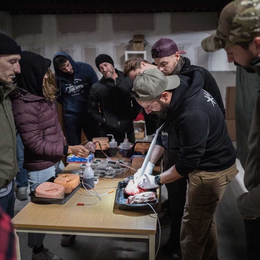  Realitätsnahes Erste-Hilfe-Training ist von großer Bedeutung, insbesondere wenn es um lebensbedrohliche Situationen und Verletzungen geht. Hier sind einige Gründe, warum realitätsnahes Training wichtig ist, sowie die Notwendigkeit von Woundpacking-Skills bei lebensbedrohlichen Blutungen in der Nähe des Körperstamms:  Stressbewältigung: In Notfallsituationen ist es entscheidend, einen klaren Kopf zu bewahren und effektiv zu handeln. Realitätsnahes Training hilft den Ersthelfern, den Stress und den Druck, den sie in solchen Situationen erleben könnten, zu bewältigen. Es ermöglicht ihnen, ihre Fähigkeiten unter realistischen Bedingungen zu üben und die erforderlichen Maßnahmen effektiv umzusetzen.  Situationsbewusstsein: Realitätsnahes Training ermöglicht es Ersthelfern, ein besseres Situationsbewusstsein zu entwickeln. Sie lernen, die Umgebung und die Bedürfnisse des Verletzten schnell zu erfassen und angemessen zu reagieren. Dies ist besonders wichtig bei lebensbedrohlichen Blutungen in der Nähe des Körperstamms, da schnelles Handeln entscheidend sein kann.  Anwendung von Woundpacking-Skills: Woundpacking bezieht sich auf die Technik des Stopfens oder Füllens einer Wunde mit geeigneten Materialien, um eine starke Blutung zu kontrollieren. Bei lebensbedrohlichen Blutungen in der Nähe des Körperstamms, wie zum Beispiel bei Verletzungen der Leistengegend oder des Bauches, kann Woundpacking eine effektive Maßnahme sein, um den Blutfluss zu stoppen und Zeit für professionelle medizinische Hilfe zu gewinnen. Durch realitätsnahes Training können Ersthelfer diese Technik erlernen und ihre Fähigkeiten verbessern, um lebensbedrohliche Blutungen zu behandeln.  Teamarbeit und Kommunikation: Realitätsnahes Training bietet die Möglichkeit zur Teamarbeit und zur Entwicklung effektiver Kommunikationsfähigkeiten. In lebensbedrohlichen Situationen ist eine koordinierte Zusammenarbeit entscheidend, um die bestmögliche Versorgung zu gewährleisten. Das Training ermöglicht es den Ersthelfern, ihre Teamfähigkeiten zu verbessern und effektiv zu kommunizieren, um die richtigen Maßnahmen zu ergreifen.  Vertrauen und Sicherheit: Durch realitätsnahes Training gewinnen Ersthelfer Vertrauen in ihre Fähigkeiten. Sie haben die Möglichkeit, in einer kontrollierten Umgebung lebensbedrohliche Szenarien zu üben und ihre Handlungssicherheit zu steigern. Dieses gestärkte Vertrauen ermöglicht es ihnen, in realen Notfällen ruhig und effektiv zu handeln.  Insgesamt ist realitätsnahes Erste-Hilfe-Training von großer Bedeutung, um Ersthelfer bestmöglich auf lebensbedrohliche Situationen vorzubereiten. Es ermöglicht ihnen, ihre Fähigkeiten zu verbessern, wichtige Techniken wie Woundpacking anzuwenden und in stressigen Situationen angemessen